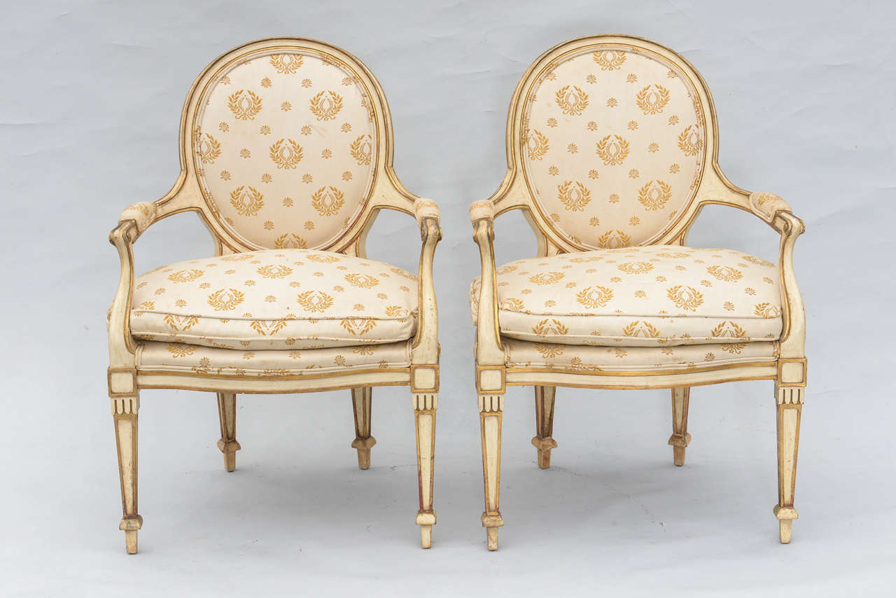Pair of armchairs, with painted and parcel gilt fielded frames, each having a rounded padded backrest, flanked by bowed arms with elbow rests, on downswept terminals, loose cushion on curving seatrail, raised on square section tapering legs, ending
