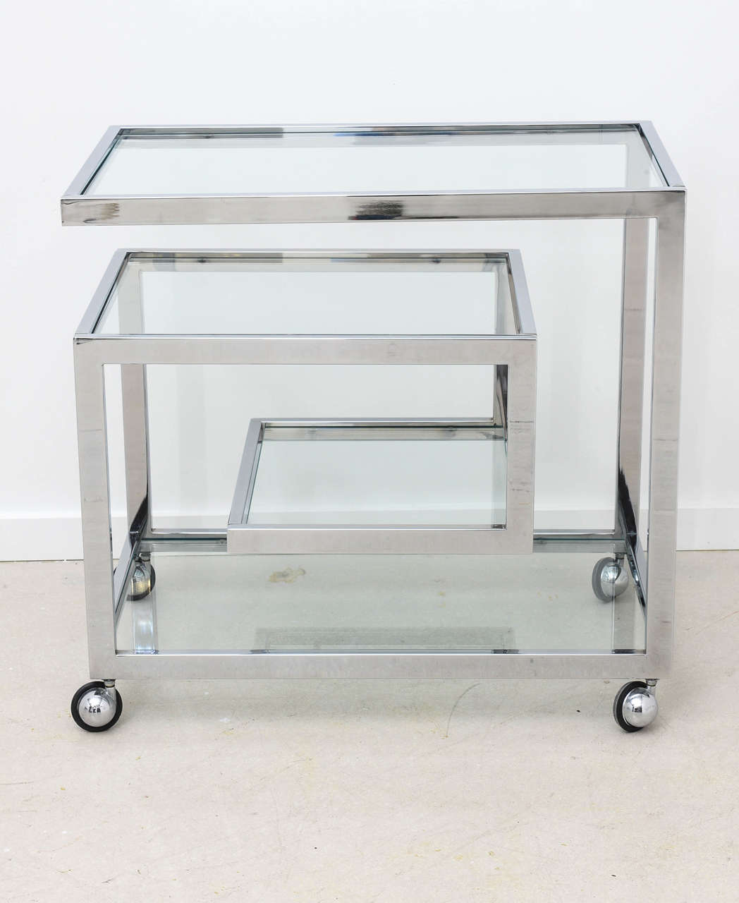 Mid-Century Modern chrome rolling bar cart with staggered glass shelves.