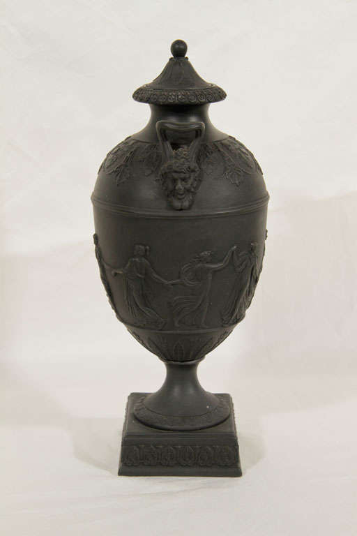 A pair of Black Basalt covered vases showing dancers in clebration. On the shoulders are acanthus leaves, palmettes and applied mask handles. The rectangular bases have a band of anthemion. The bottom of each vase is marked 