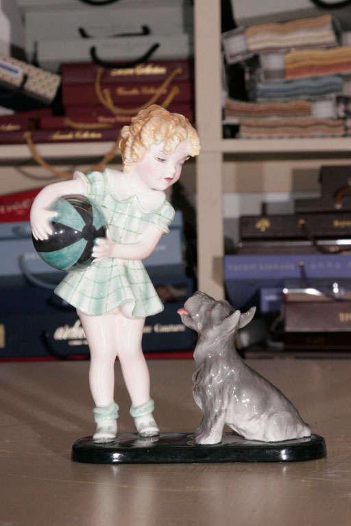 A Goldscheider Figure of a Girl with a terrier, wearing a checked dress, holding a large blue and green striped ball. On an oblong black glazed base.
Impressed marks- 7825/148 and 31.
Decorators Mark AN.
