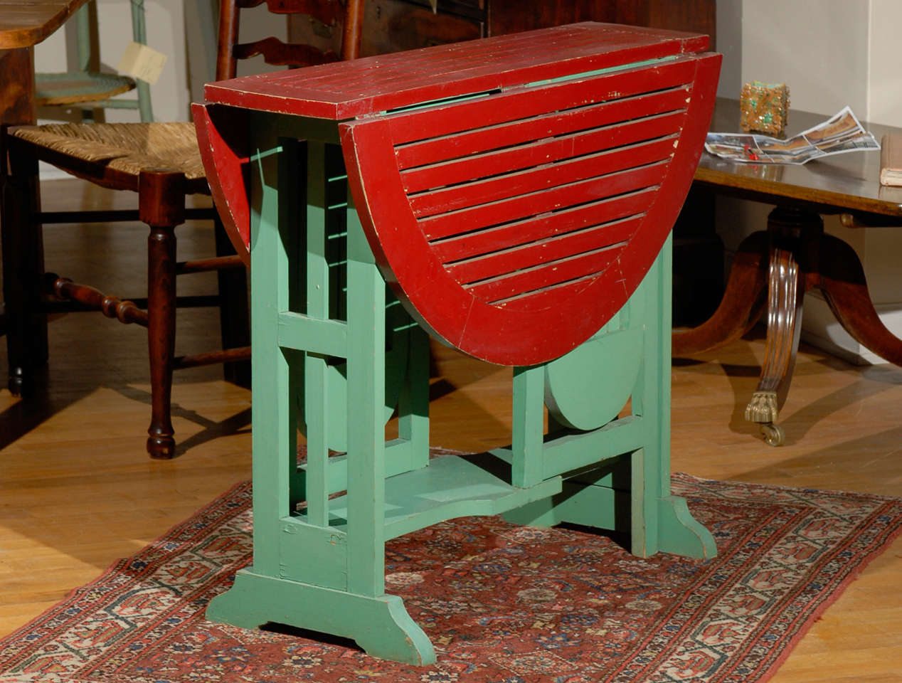 This is a fabulous table.  The table is in the gate leg style.  The soft green legs fold out for either a round table or semicircle table.  There are two small shelf like stands underneath the two gates.
This table is a wonderful piece of