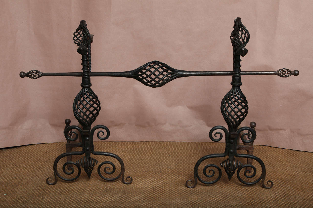 A pair of Arts and Crafts andirons with open wrought iron twist work bodies and scrolled supports with finials, and pivoting spit supports, retaining original matching spit. Impressive design and scale.
