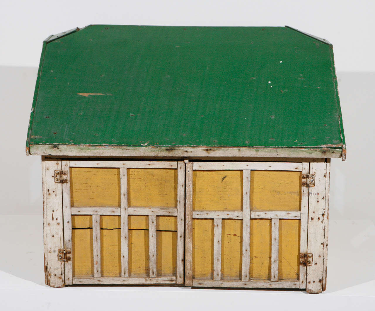 A wooden architectural model in original paint of a garage or barn structure, likely used as a child's play object, with a single door and three windows, along with a highly detailed set of double doors, which open on hinges. Made of scrap wood,
