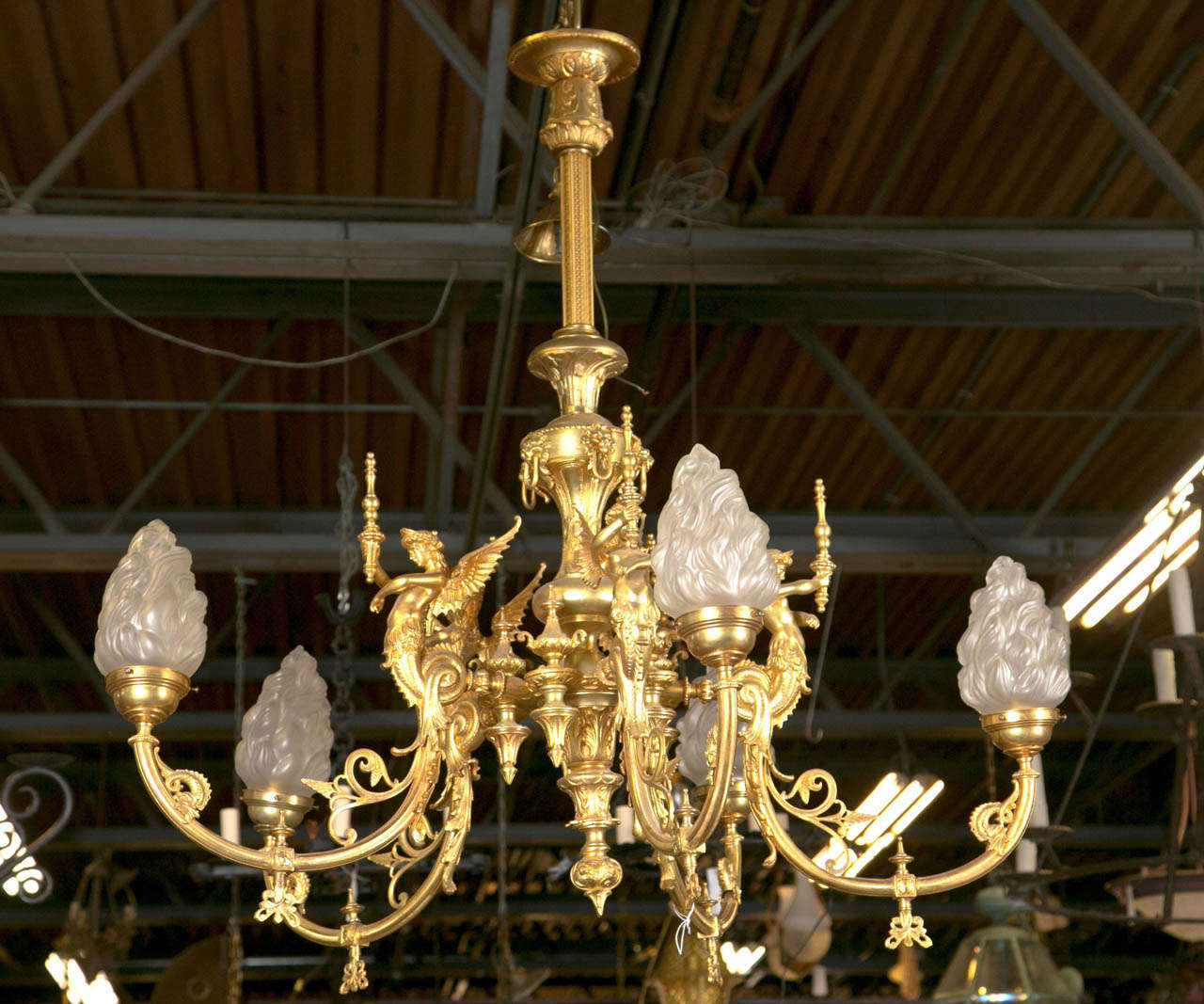 This chandelier is an old gas fixture converted to electric. It is a bronze five arm fixture depicting goddess bodies (like mermaids with wings). Each fairy like goddess is holding a torch.  Surrounding the winged goddess are acanthus leaves in