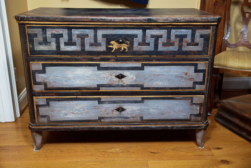 early 19th century Biedermeier three drawer chest finishing on flared feet and adorned with a lion in hues of white grey and teal gray, drawers glide easily open with use of keys as pulls.

 to view additional items from this dealer, click on