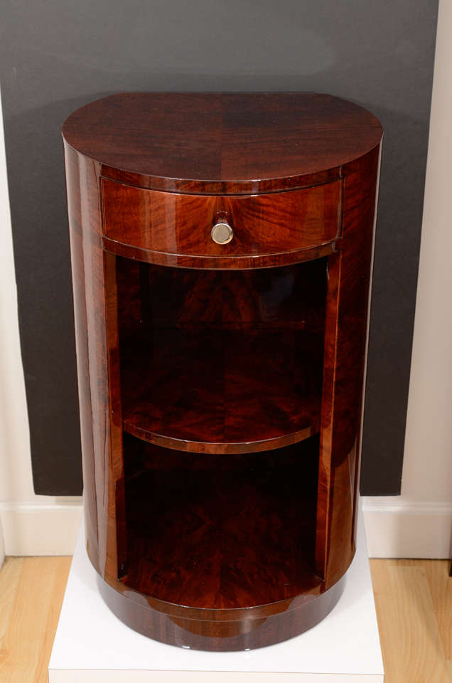 A pair of machine age Art Deco round nightstands in the style of Gilbert Rohde. Made of myrtle burl veneer and East Indian laurel veneer. Top drawer has polished chrome hardware and two open shelves on the bottom.