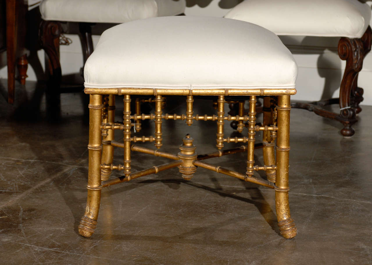 This French Empire style upholstered stool, circa 1870 features a giltwood framework in Asian inspired form and rests on four faux bamboo legs connected to one another by a cross stretcher. A characteristic of the French Empire period was the taste