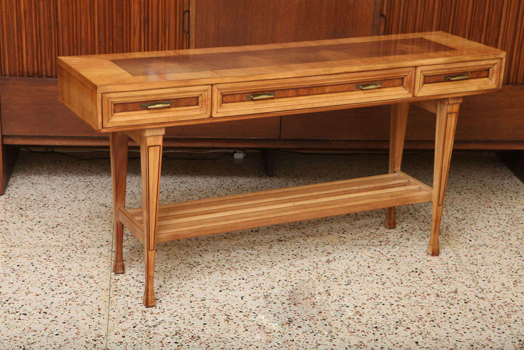 ....SOLD OCTOBER 2012...Wonderfully proportioned and beautifully styled modern bleached mahogany with burlwood inlay three drawer console table.  Richly detailed with inlay and incised stringing, molded slat stretcher shelf and stylised hoof feet. 