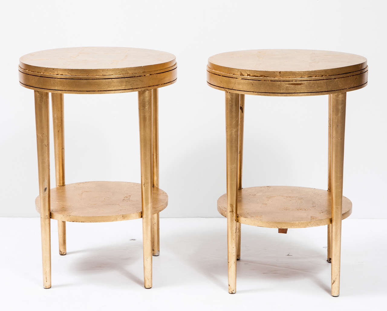 A chic and stylish pair of giltwood round side tables with lower shelf and slightly tapered legs.