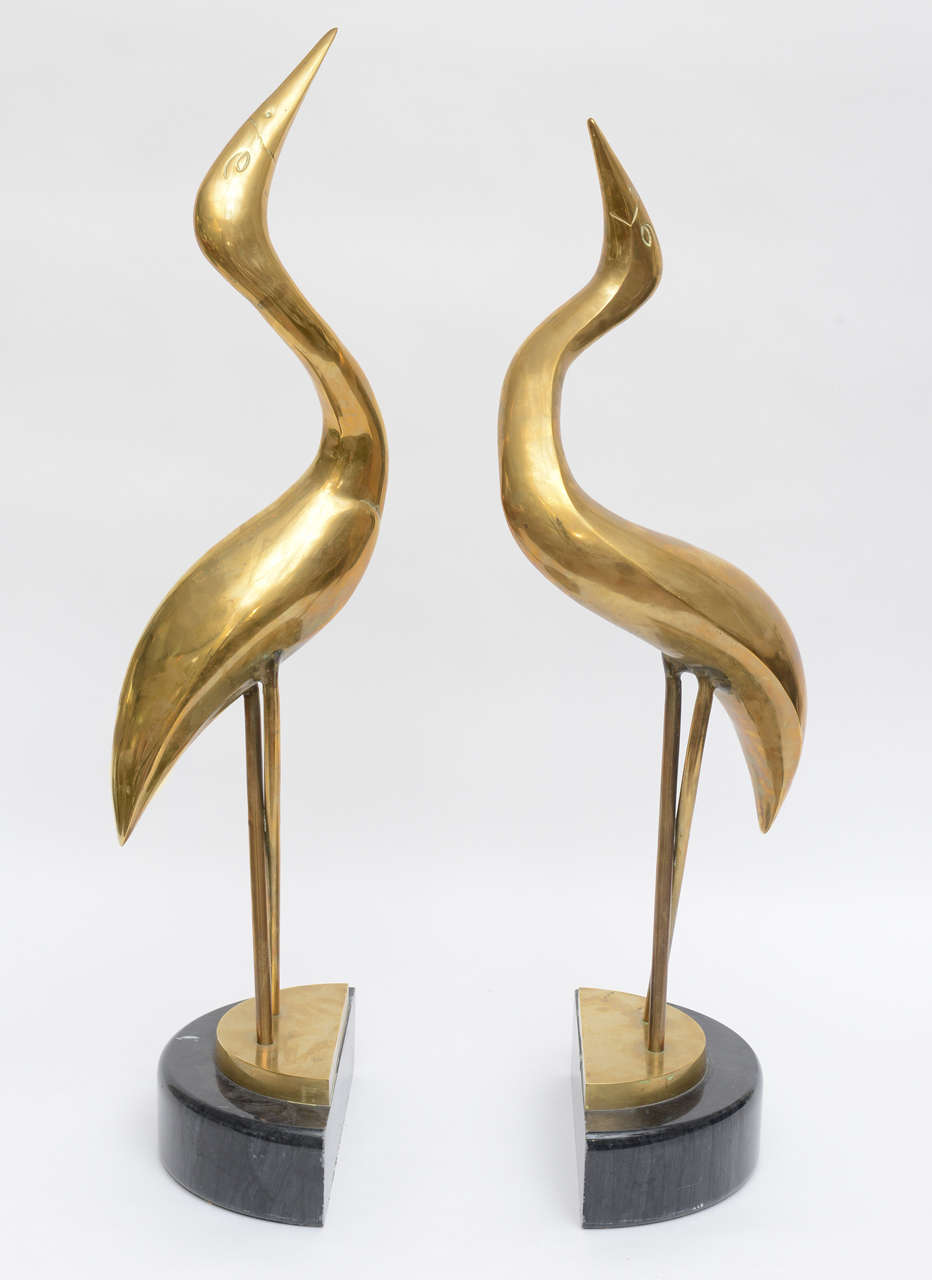 Solid brass modernist-style herons mounted on semi-circular, half-moon shaped black marble bases, with the look of replete, enlightenment.
