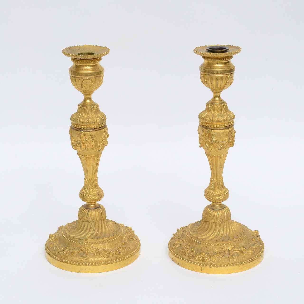 Pair of monumental 18th century, French gilt bronze candleholders, with festooned garland surround to perimeter base, assorted leaf design details throughout, with fluting, hobnail dots, and topped up with small scalloping to perimeter top of