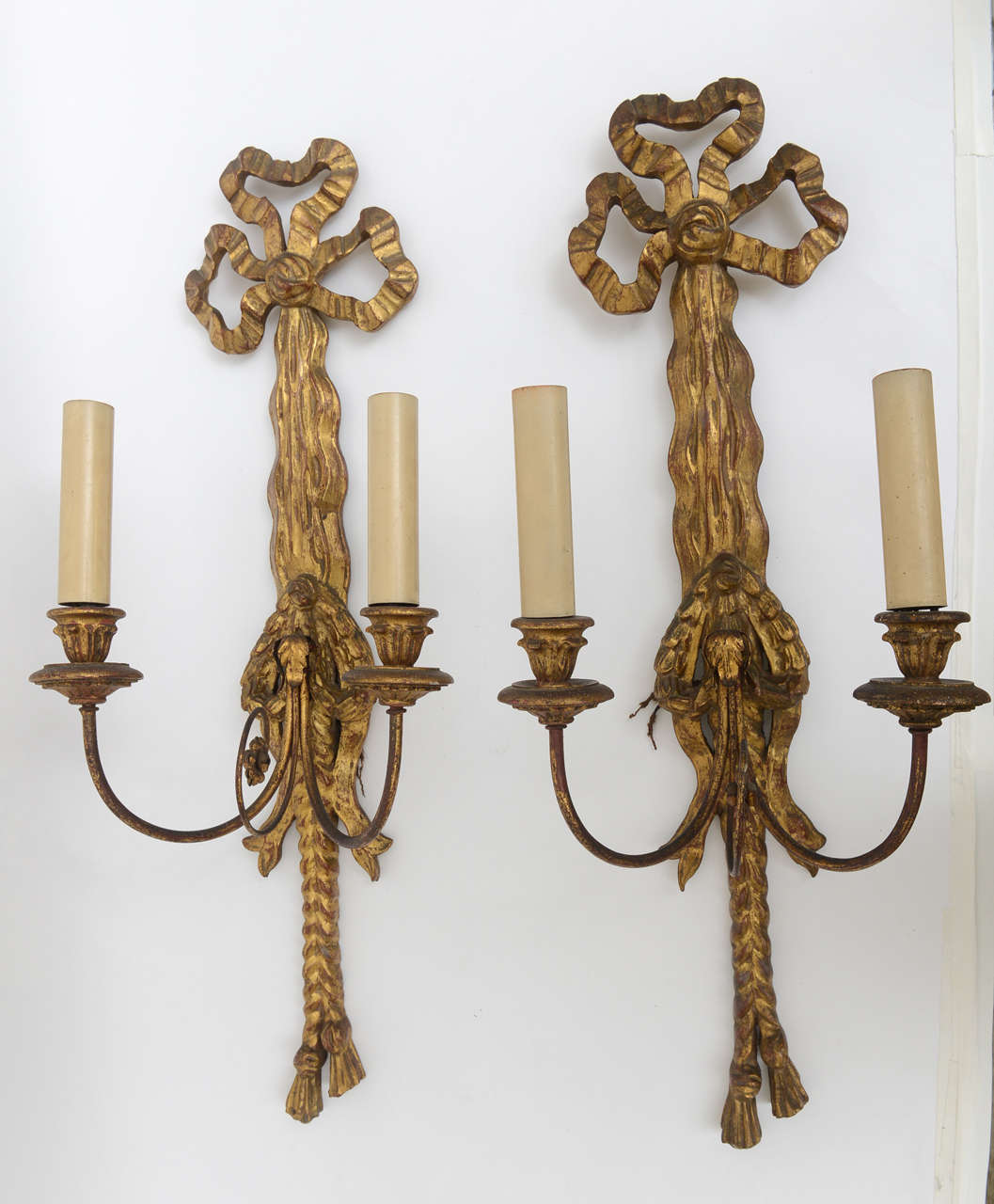 1930s pair of hand-carved wood detailed and brass, two-arm candlestick sconces. Hand-carved wood tassel-roped details, with crimped, festooned bows. Newly re-wired and in working condition. Brass elements are the looped arm extensions of the