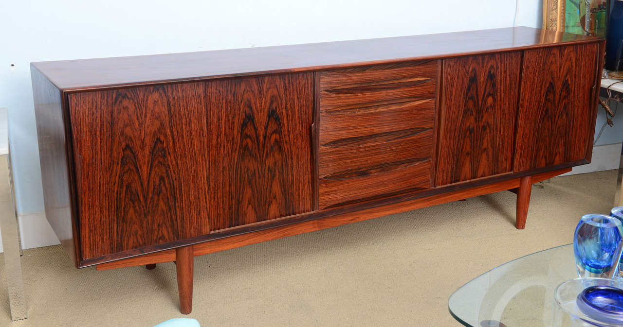 Amazing hi-end rosewood Danish sideboard dating back to the 1960s. This piece is in beautiful condition. In the center it houses a set of five drawers that go from smaller to largest as they go from top to bottom, the sides have sliding doors with a