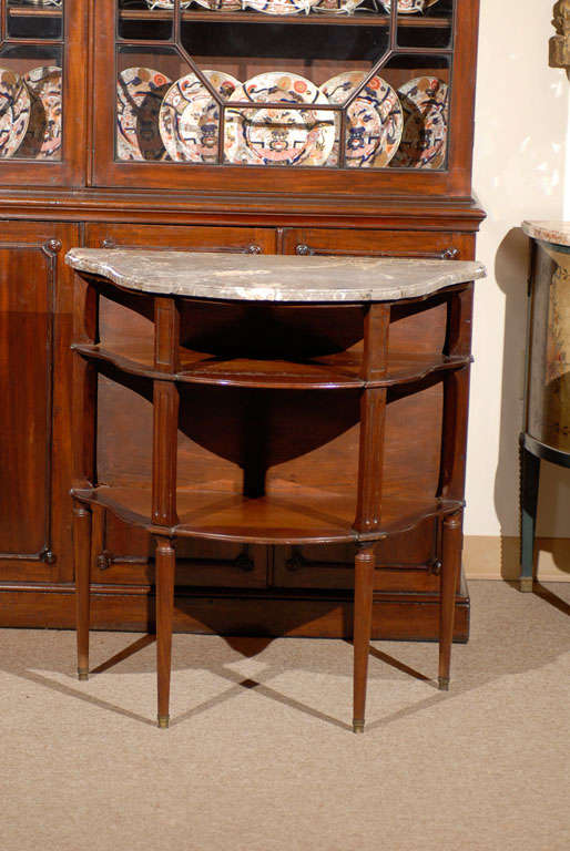 A mahogany dessert table with shaped marble top with 2 shelves below with fluted supports. All resting on circular tapered legs with brass feet. 

William Word Fine Antiques: Atlanta's source for antique interiors since 1956.