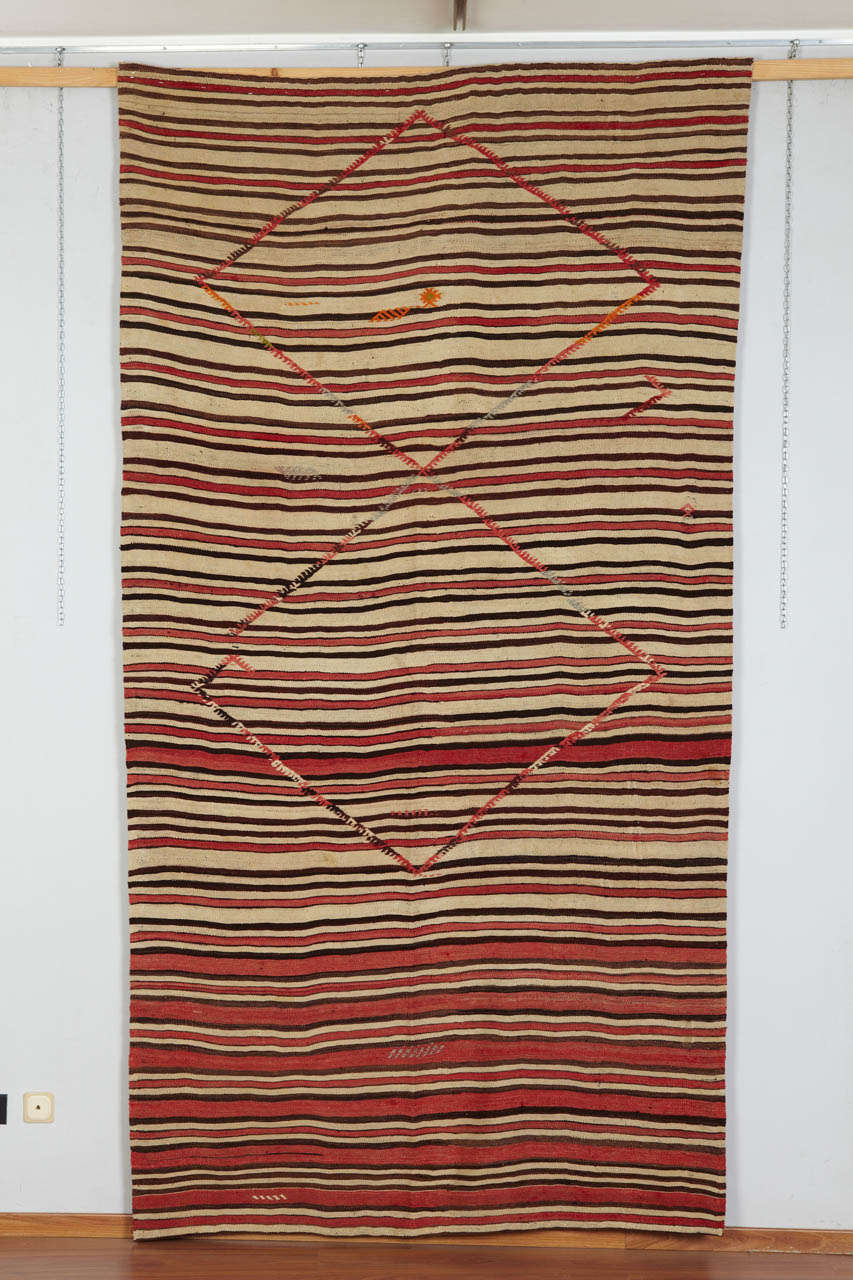 Village Anatolian kilim. This rug is a big motif of elibelinde and some small embroidered motifs, on a striped field: cream, brown and brick red. The color variation of the rows is amazing. This rug is an authentic village production.