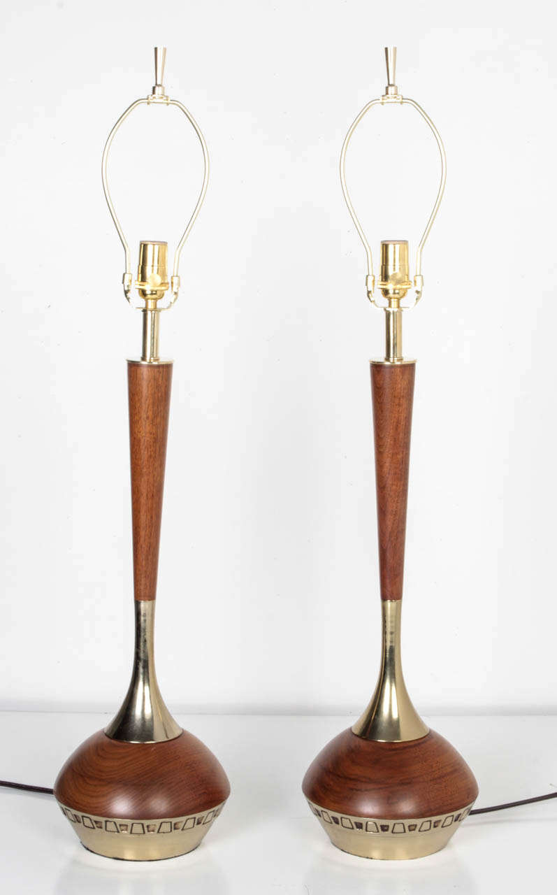 ATL1866
A pair of teak wood lamps with tapered cylindrical bodies on cast metal bases with incised geometric details in a lacquered polished brass finish. Circa 1960s.

Dimensions:
Overall: 35