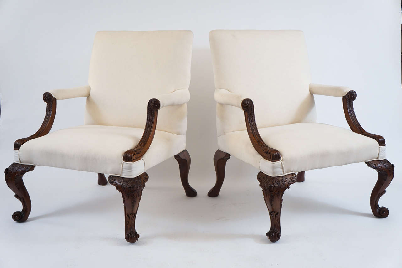 A truly outstanding pair of English, mid-George II style 'Gainsborough' armchairs having exquisitely carved mahogany frames with rectangular padded backs, seats, and arms flanked by down curved interlacement-band and acanthus-sheathed armrest