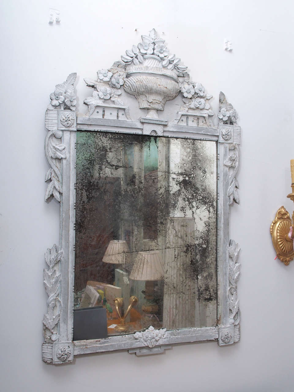 Carved wood and painted Louis mirror is painted white and grey. The paint is worn and faded, which emphasizes the carved wood designs.  The paint and wood are cracked and crusty looking in certain areas.  The mirror is dark and rubbed off