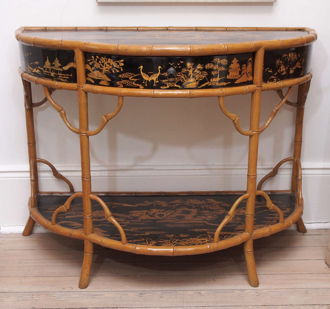 This charming pair of bamboo and chinoisserie console tables are from mid 19th century England.  The natural, camel colored bamboo frames a black chinoiserie painted table top, one pull out drawer and bottom shelf.