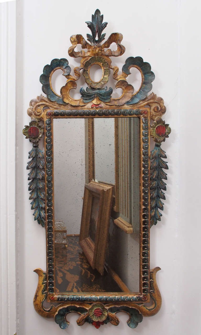 Gilt, polychrome, and painted mirror is framed with carved, painted ribbons and fern shaped leaves.