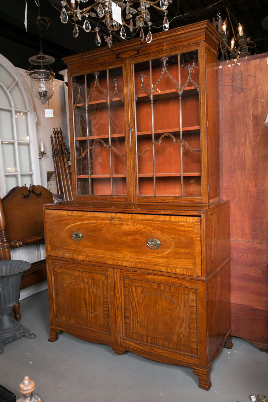 A c. 1790 George III satinwood bookcase with a fitted secretarie drawer, over a pair of oval paneled doors with scalloped apron and high bracket feet.