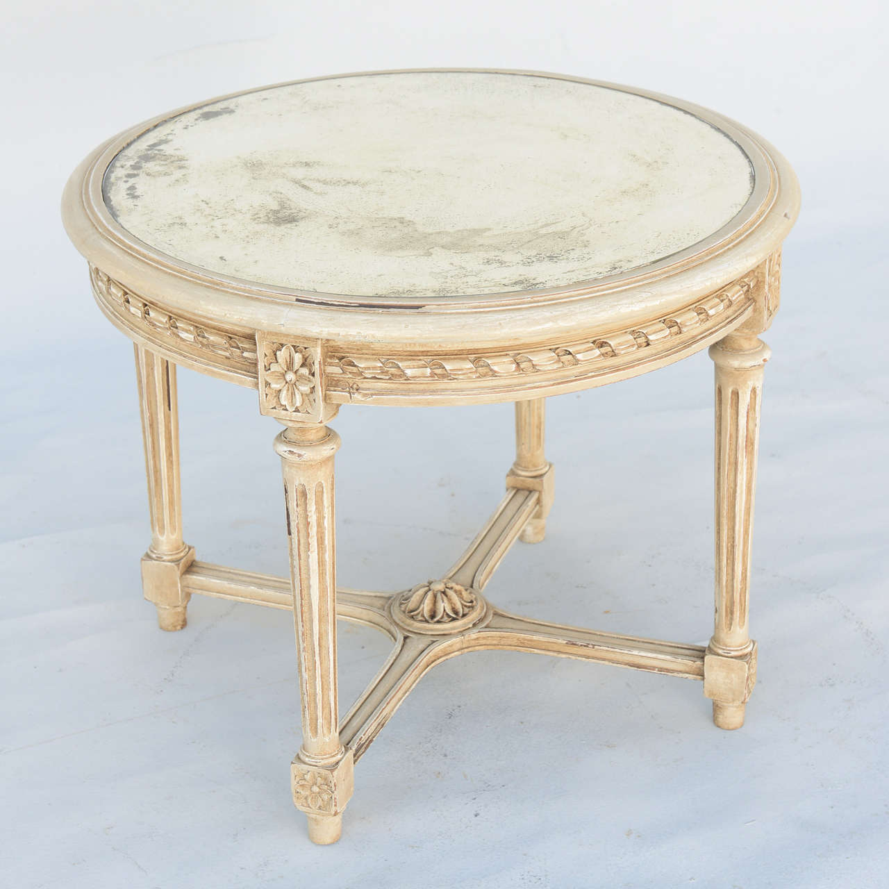 Table, with round top of distressed mirror, on carved and painted base decorated with gadrooning and beading, raised on round, fluted legs joined by double stretcher centered with a rosette.

Stock ID: D7185