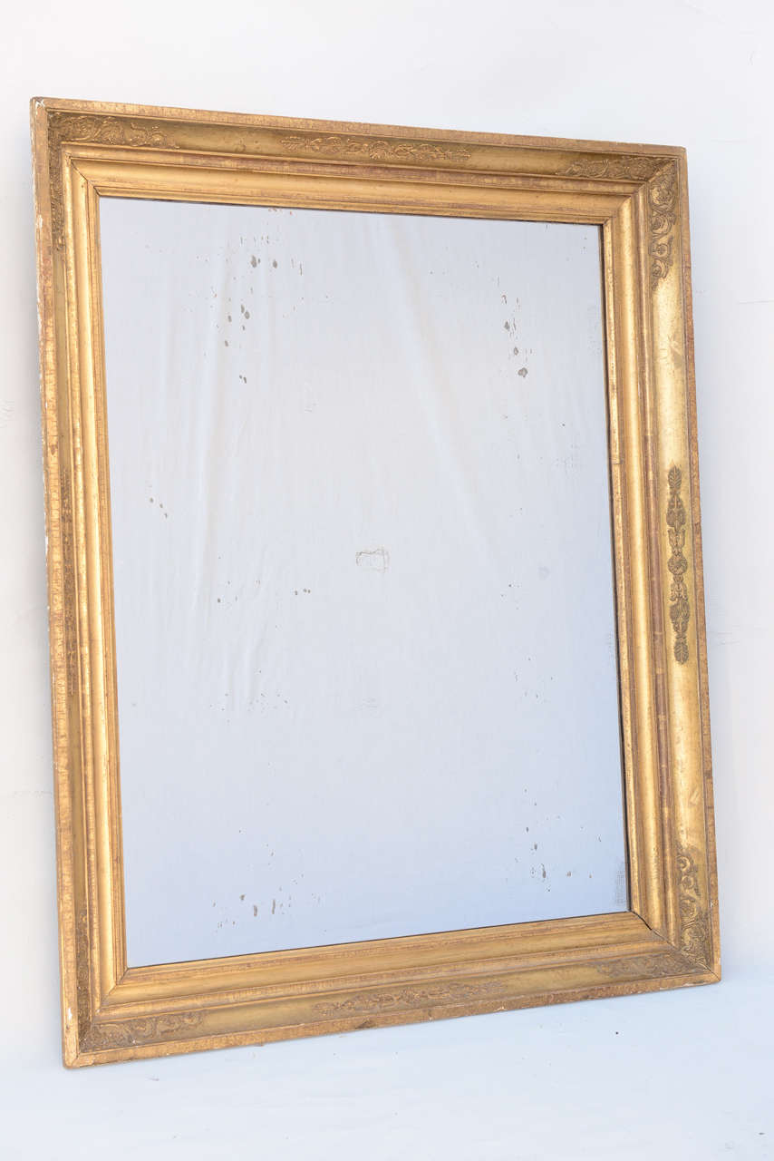 Empire period mirror, of gilded wood and gesso with a neoclassical style, having a molded frame decorated with palmette, foliated scrolls, and rosettes.