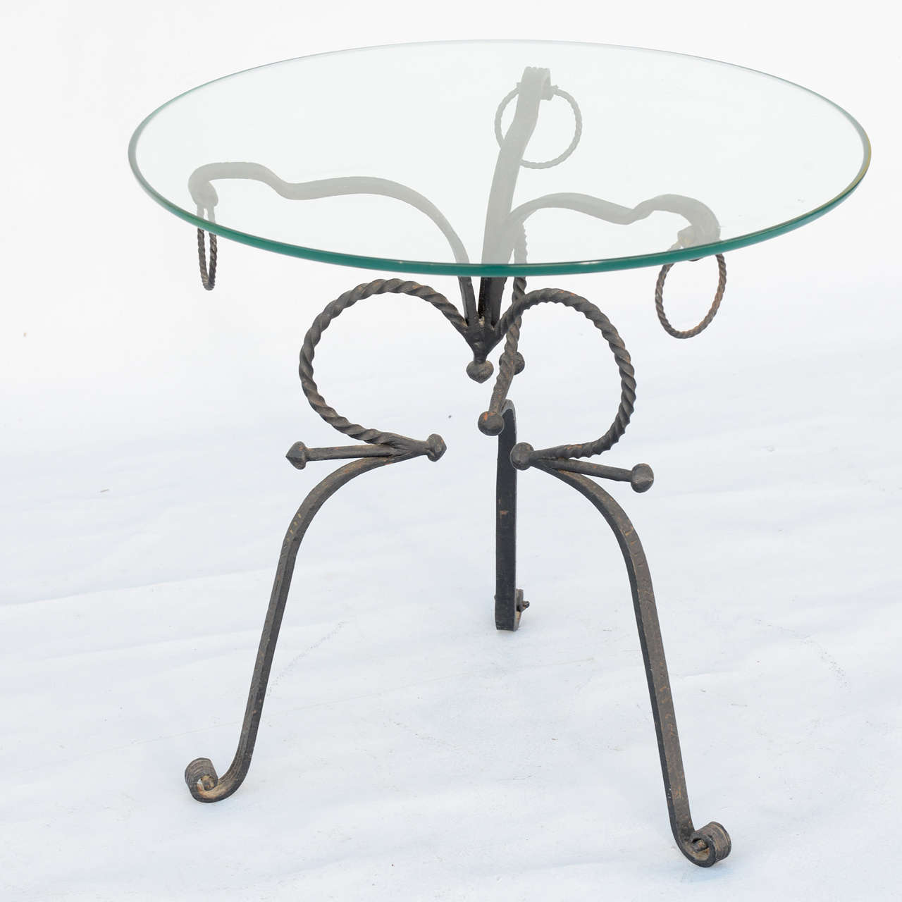 Occasional table, having a top of round glass, on tripartite base of scrolling hand-wrought iron, each hock-leg decorated by rings and ending in scroll feet.

Stock ID: D3246