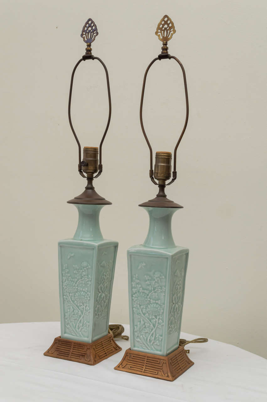 Pair of early 20th C. Chinese poreclain pale celadon lamps. Unusual tapered panel flat sides. High relief decorations of chrysanthemums, lotus and butterflies depicting changing season. Finials. Custom hand carved wooden tapered bases with stylized