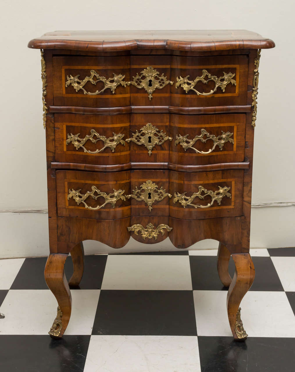 Diminutive 18th century German walnut Rococo commode. Stylish shaped top and front with figured walnut veneers. crossbanded top and drawers all fitted with gilt brass mounts. Three well-proportioned drawers over stout cabriole legs. Refinished,