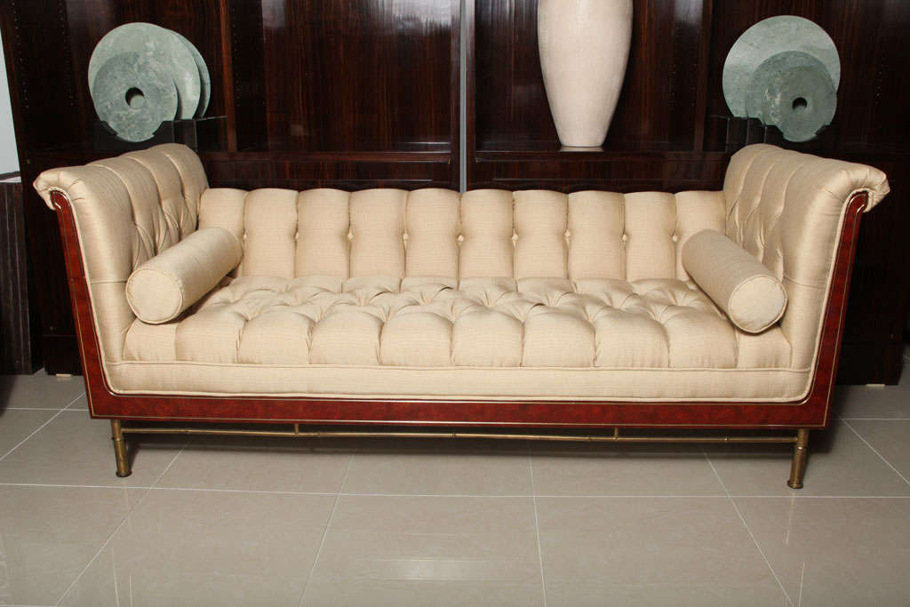 the burlwood frame with brass panels on reeded brass legs and stretcher, the whole upholstered with tufting