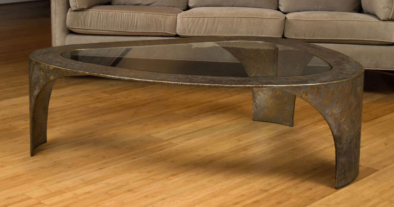 Une table basse brutaliste de Silas Seandel. Cadre en métal brossé avec trois pieds épais et un plateau en verre asymétrique.