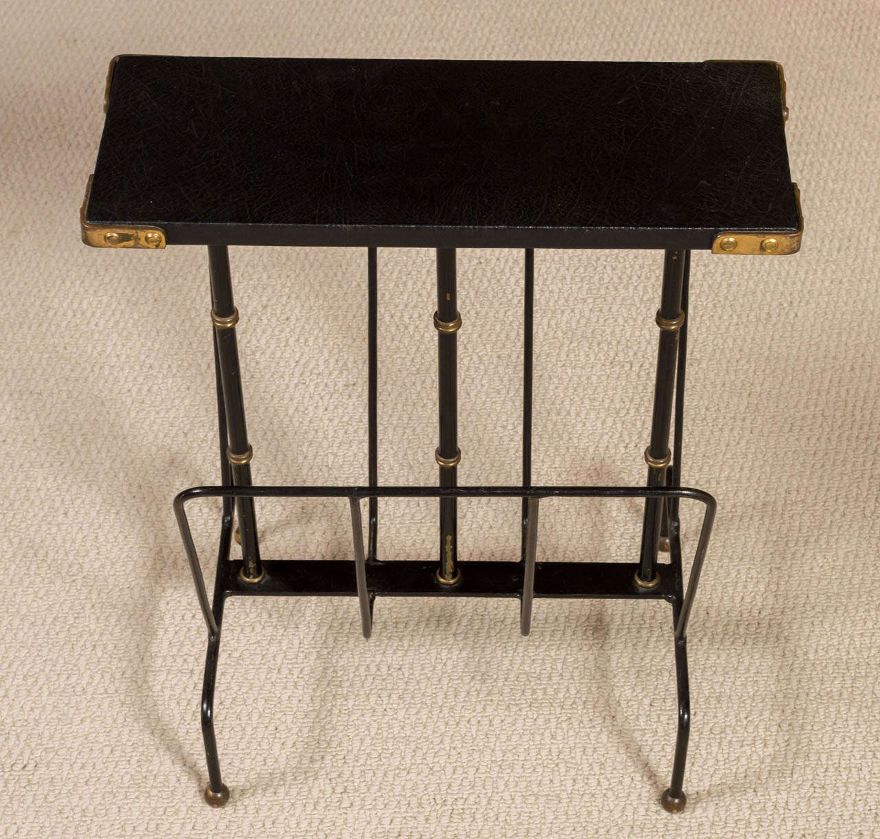 A magazine rack or side table, in painted metal with leather-covered top and brass detailing by Jacques Adnet, France, circa 1960.