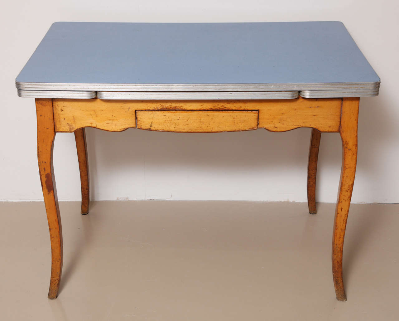 The pale blue formica top with two retractable leaves over a small frieze drawer. Could be used as a kitchen table or as desk. Very attractive glowing wood.