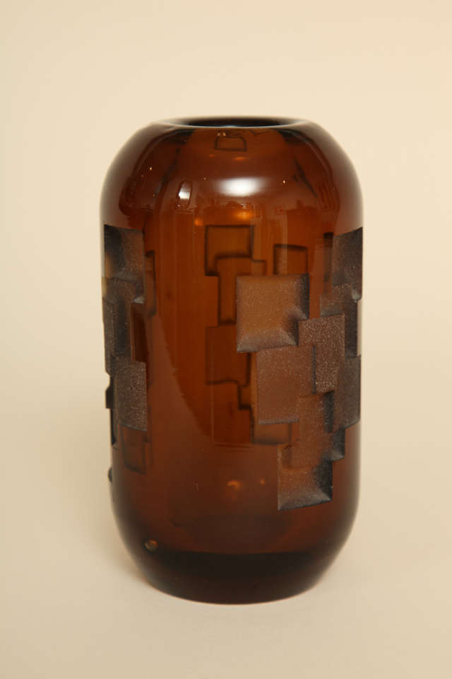 This amber glass vase has overlapping etched squares with repeated decoration around the body

Jean Luce (1895-1964) worked as a designer in a cubist-inspired style, rejecting the use of too much design and figurativeness in decoration. He