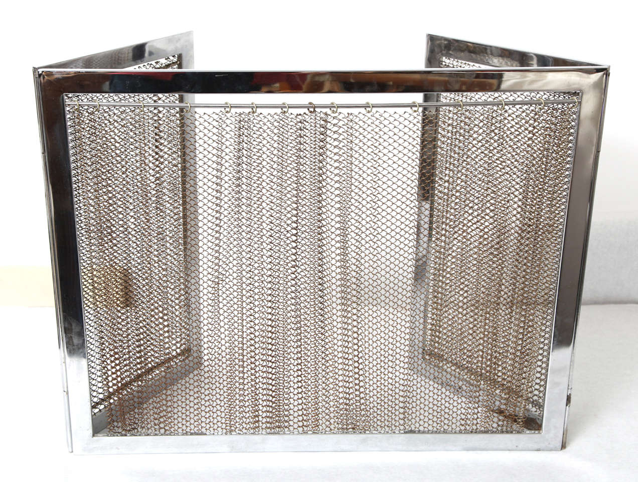 A chrome fireplace screen with metal mesh. Central panel and two collapsible lateral panels. Curtain-style mesh. 