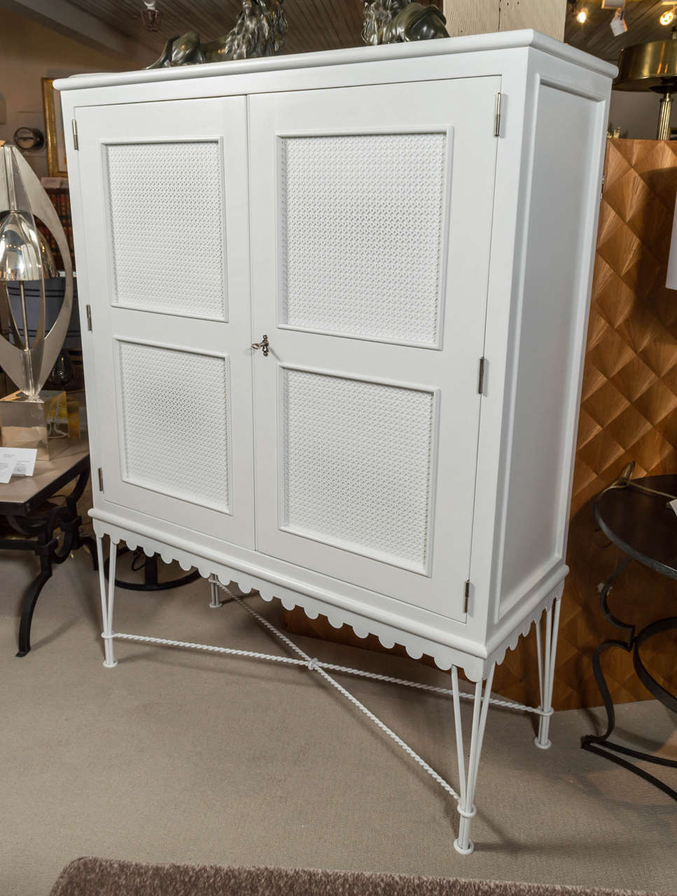 A white-painted, two-door cabinet attributed to Gilbert POILLERAT, featuring latticework panels and mounted on a decorative, wrought-iron base.
France - circa 1940