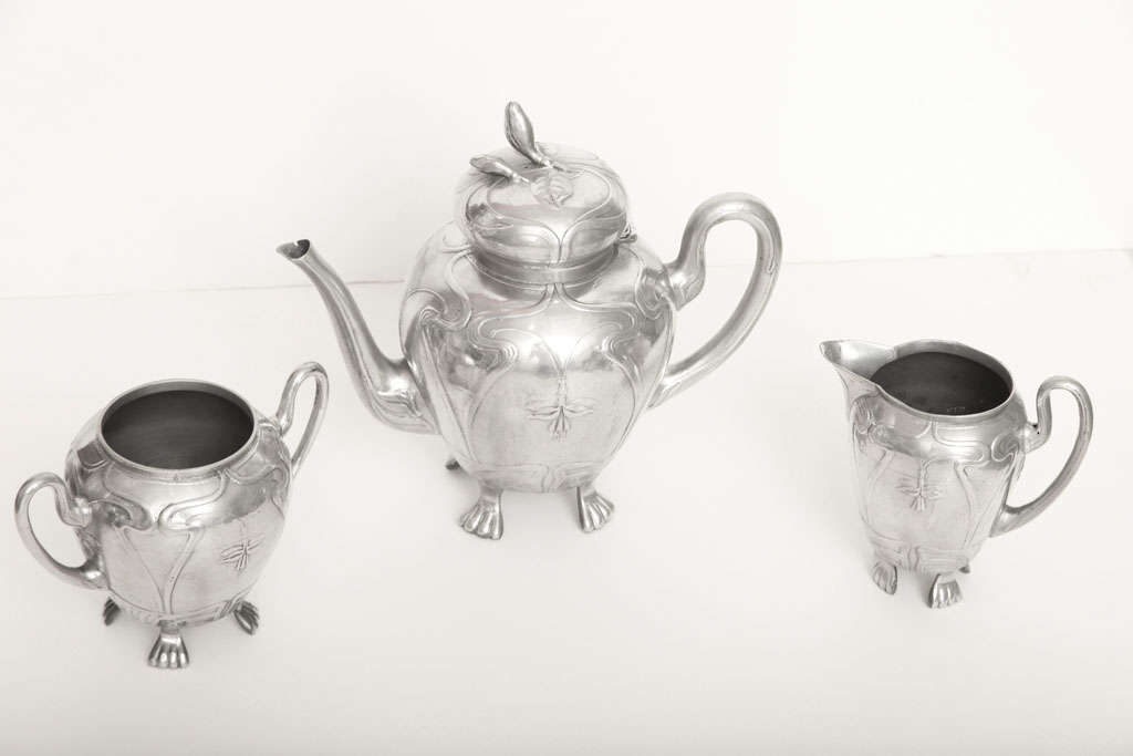 This whimsical Art Nouveau German tea service consists of a covered tea pot, creamer, and sugar bowl. They are incised with Art Nouveau inspired details. Each piece features four humanistic feet that further adorn and elevate the design.