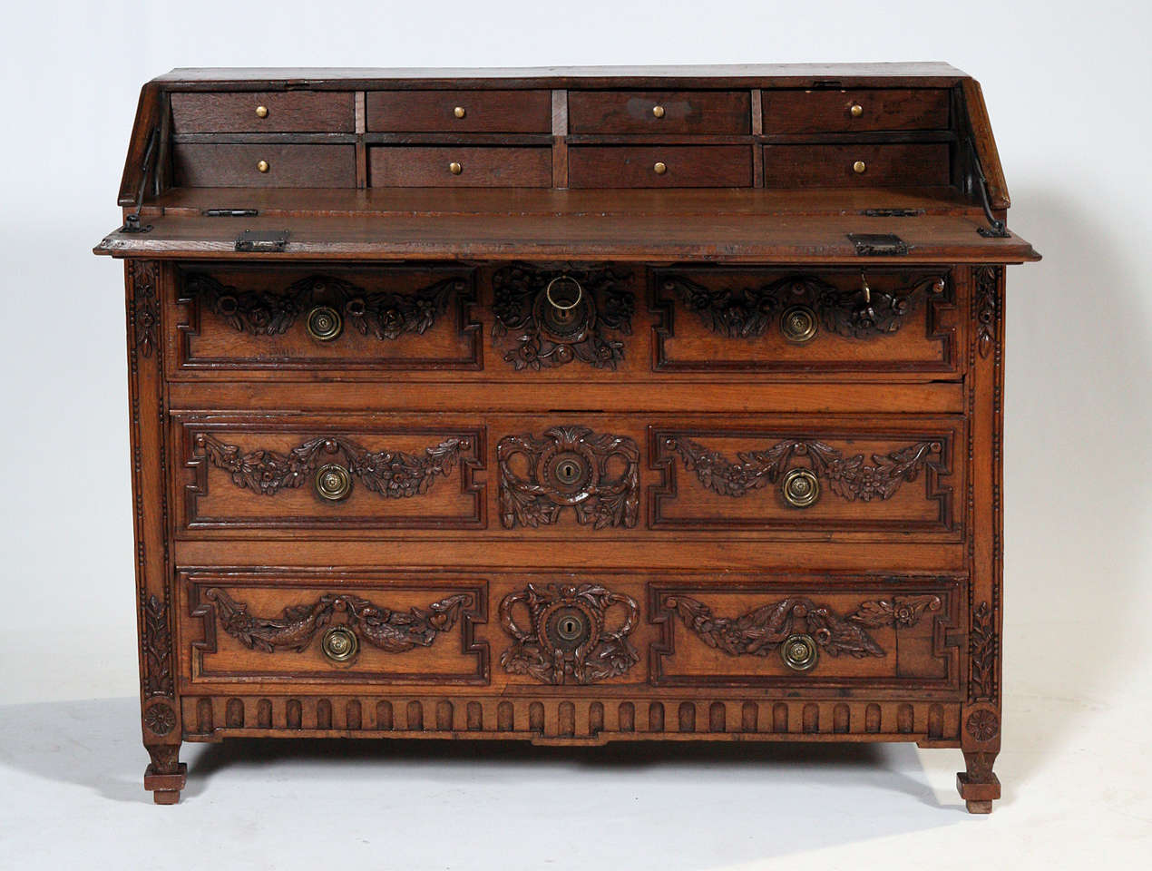 An elegant Louis XVI style white oak provincial desk commode. This piece is decorated with amazing raised carvings of laurel swags and floral designs. This is cleverly repeated from the slant down to the three drawers. Centered is a finely