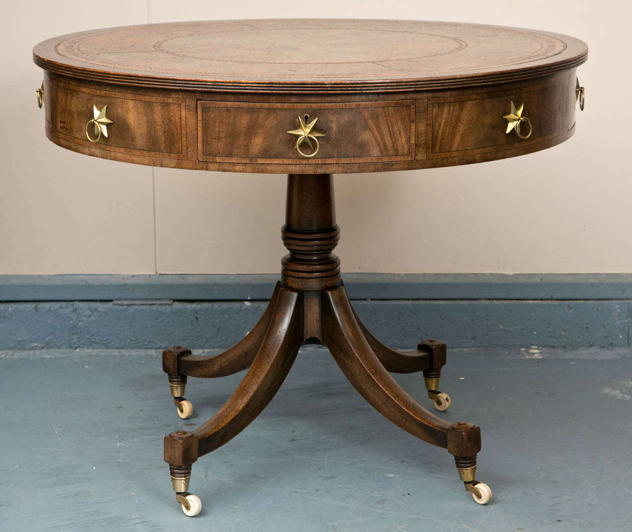 This attractive rent / drum table has wonderful proportions and shows its age beautifully. Brass ring drawer pulls with star back plates are an attractive touch that gives the table a unique look in a subtle departure from the norm. The leather top