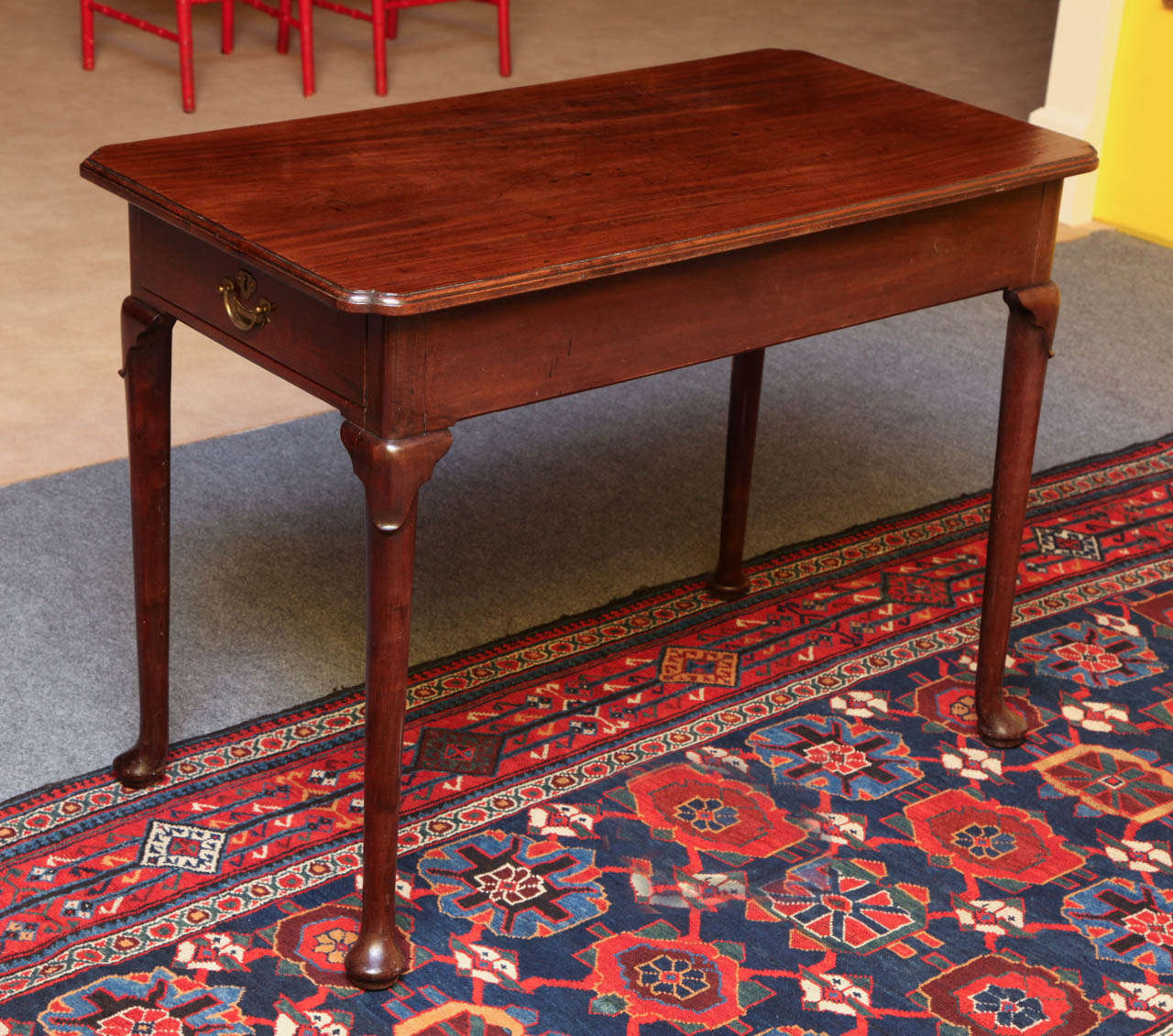 Very fine George II period carved mahogany center table, the solid overhang molded top with re-entrent corners, with one drawer to either narrow end and a plain frieze, finished on all sides and raised on turned cabriole legs with lappet carved