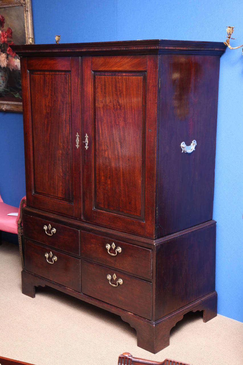 Chippendale period mahogany cabinet on chest or clothes press with wonderful color and pagination, having a dentil carved cornice above a pair of fielded panelled doors opening to a plain interior, the lower section with four short graduated drawers