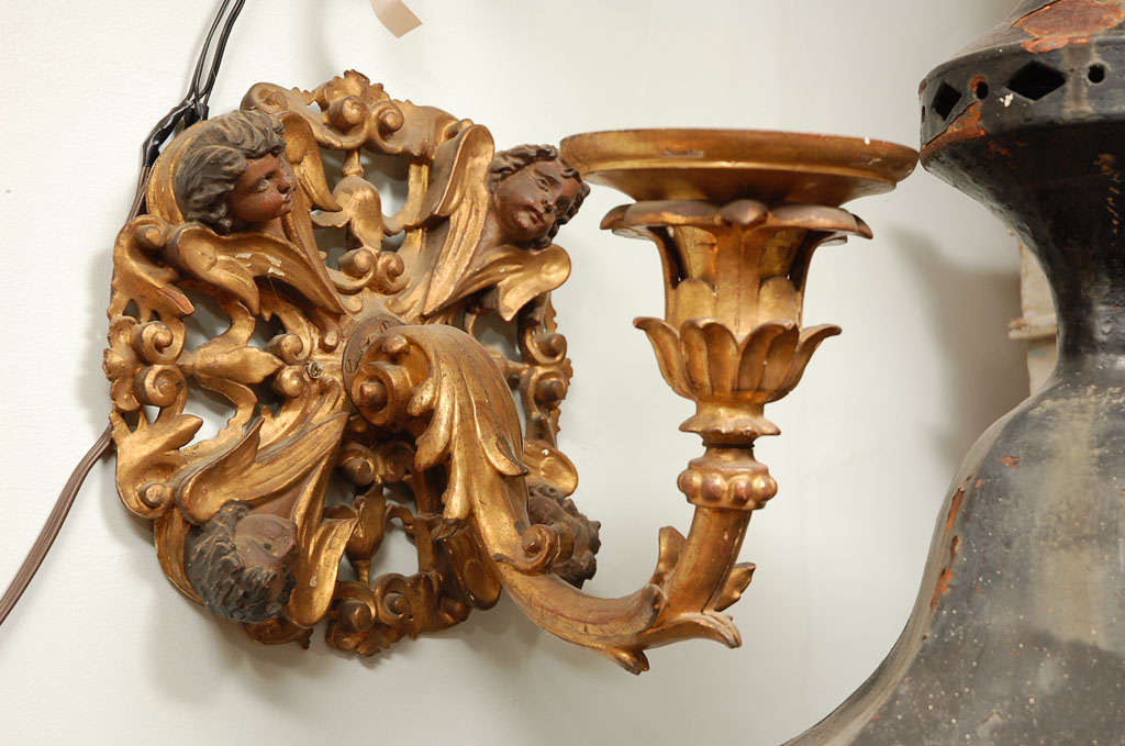 Pair of Italian 19th century hand carved wood single arm candle sconces. Wall plaque carved with four angel faces and wings converging in the center, at the base of the sconce arm. Floral decoration throughout. Original gilt and paint.  For candles.
