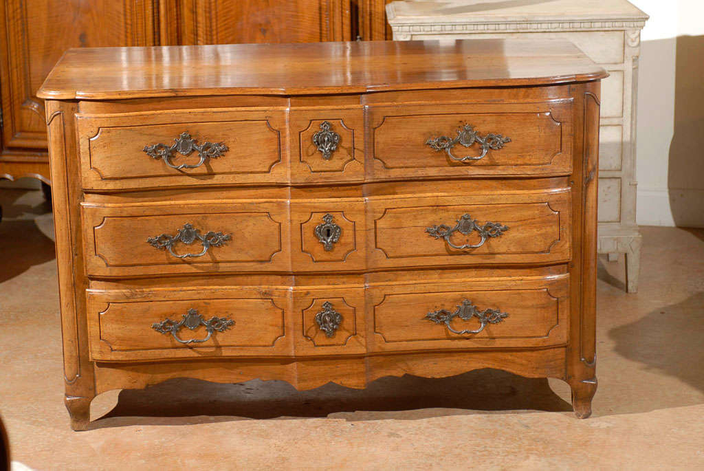 A French Louis XV period walnut commode en arbalète with three-drawers and panelled sides from the mid-18th century. This French three-drawer walnut commode features a shaped top sitting above a crossbow facade. Three hand-cut dovetailed drawers are