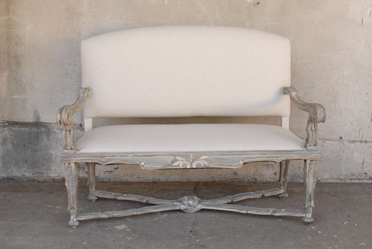 An Italian 19th century Rococo style painted wood upholstered settee with scroll arms, profiled cross stretcher with mask carving and floral carving on the skirt.