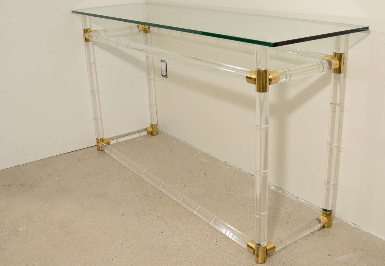 Timeless and exceptional, this Lucite console table has polished brass joints with a rectangular glass top. The Lucite is molded in a faux bamboo style. 

Charles Hollis Jones is an American artist and furniture designer who is currently being