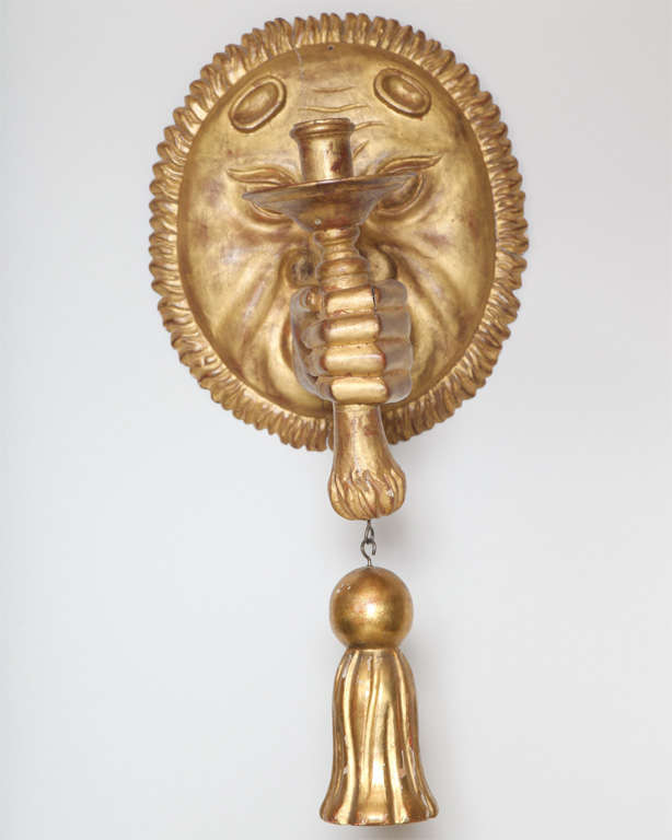 Single carved giltwood sconce, in unusual shape, of sun with arm extending from mouth, holding a torch with a tassel. Not electrified. 