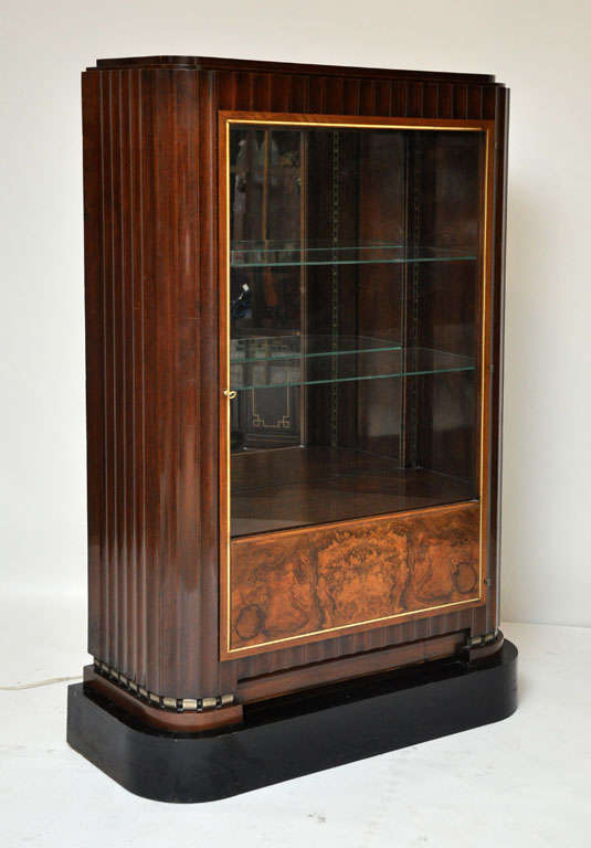 French walnut Art Deco curio cabinet in the style of French designer Emile-Jaques Ruhlmann(1879-1933).  Fluted rounded sides connect ivory framed glass door revealing lighted interior with glass shelves and mirrored back panel, bottom shelf with