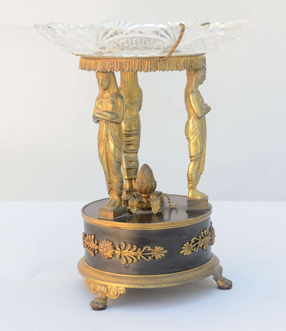 Fine period Empire tazza, having a bowl of cut lead crystal supported by a trio of caryatids standing on a round plinth decorated with anthemion flanked rosettes, over chased bronze base, raised on paw feet.

Stock ID: D6233