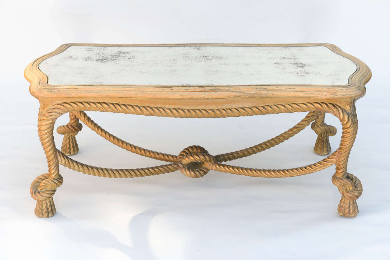 Coffee table,having a free-form top of distressed mirror, on conforming base with painted finish showing natural wear, raised on legs carved as ropes, with open knots, ending in tassels, joined by four swag ropes with a central knot.

Stock ID: D7148